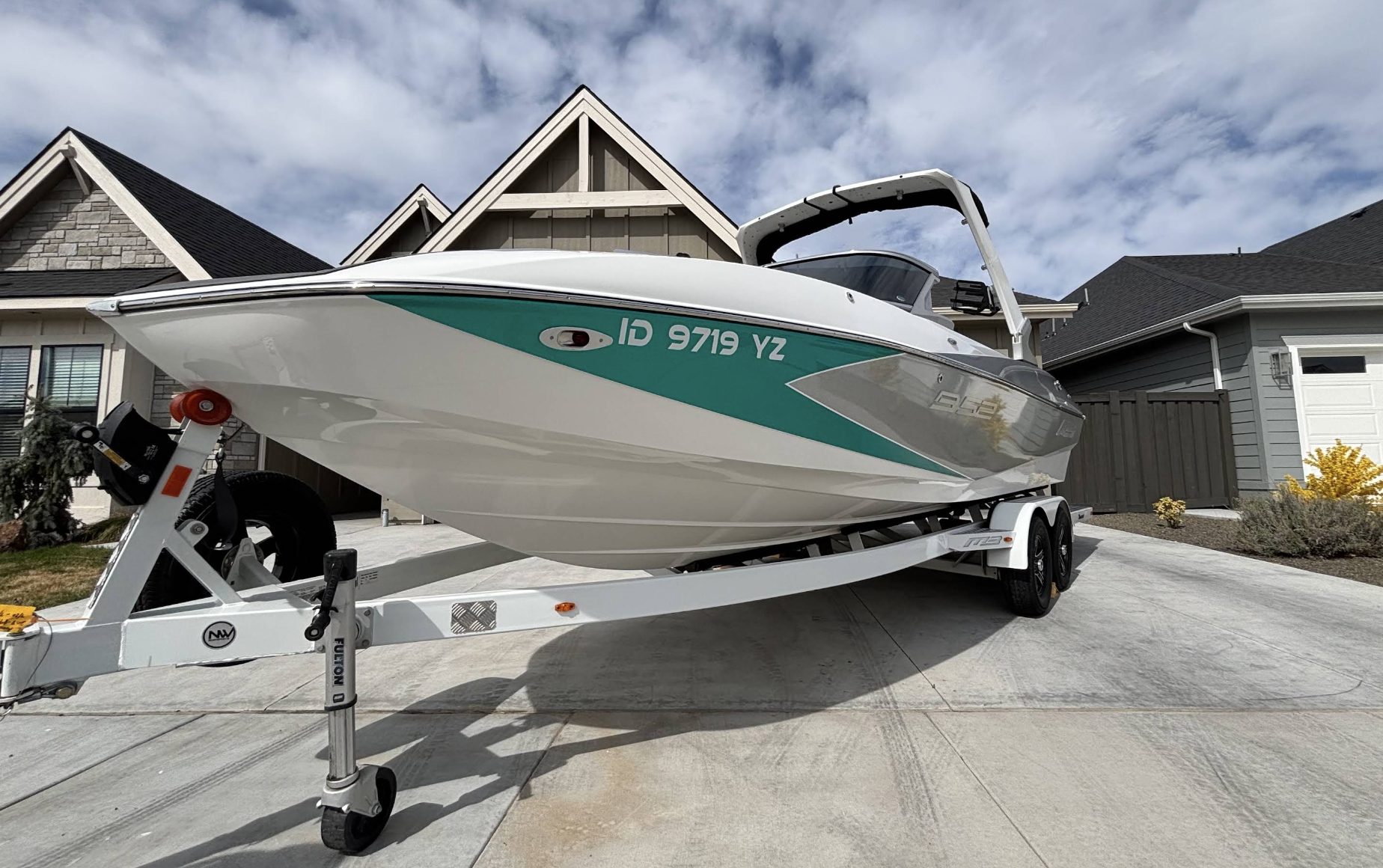 Detailed teal and white wakeboard boat on its trailer in a clean residential driveway